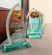 Glass trophy with several similar glass trophies behind it. Inscription reads 2020 Legacy Award, Financial Operations, Florida Tax Collector's, Inc. Hon. Ken Burton, Manatee County.